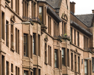 View of traditional Scottish sandstone tenement buildings with bay windows and decorative details under an overcast sky.