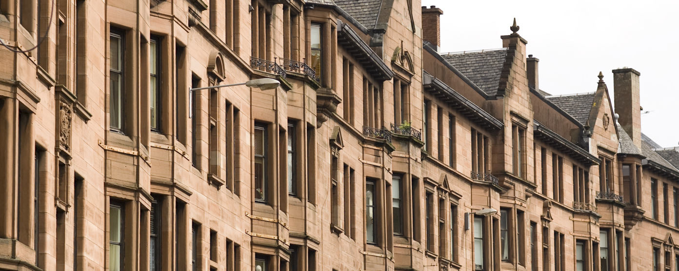 View of traditional Scottish sandstone tenement buildings with bay windows and decorative details under an overcast sky.