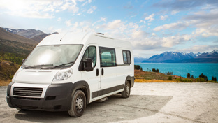 White campervan parked by a turquoise lake with mountain and valley views under a partly cloudy sky