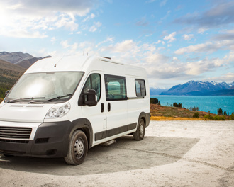 White campervan parked by a turquoise lake with mountain and valley views under a partly cloudy sky