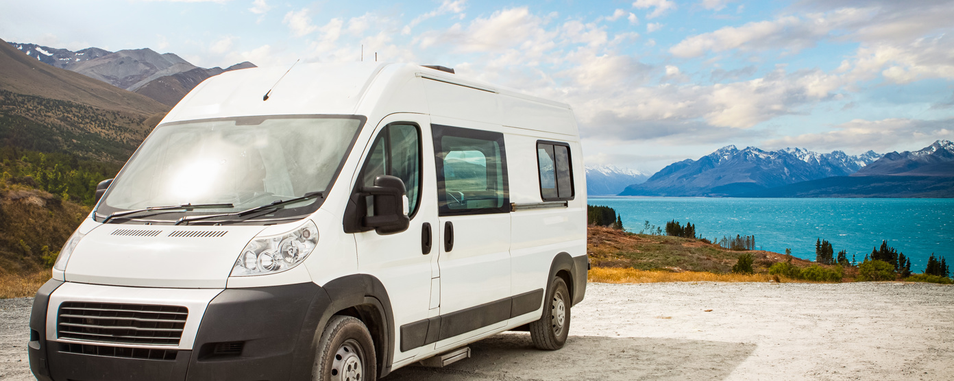 White campervan parked by a turquoise lake with mountain and valley views under a partly cloudy sky