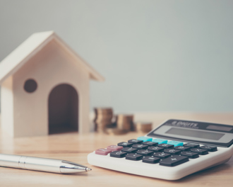 A calculator, pen, coin stacks, and a house model represent home finance, budgeting, and property investment calculations.