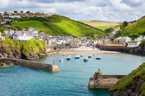 Cornish harbor with small boats, green cliffs, and a village around a sheltered bay.