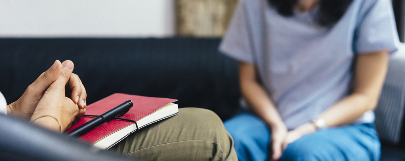 Close-up view of a therapy or counseling session, showing a therapist with a notebook and a client sitting across