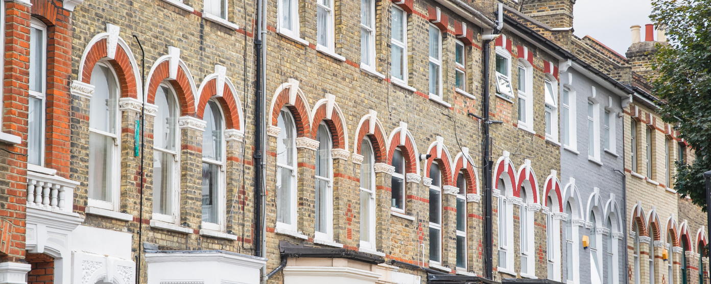 Row of traditional brick terraced houses in the UK with "LET" and "FOR SALE" signs, indicating properties on the market.