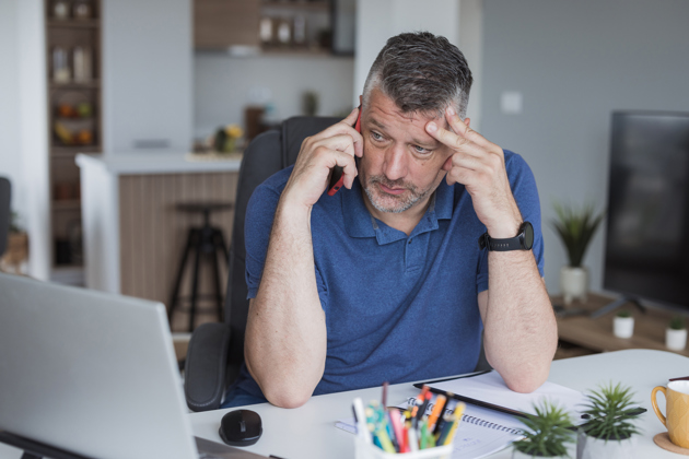 Anxious looking man on a mobile phone at his computer desk