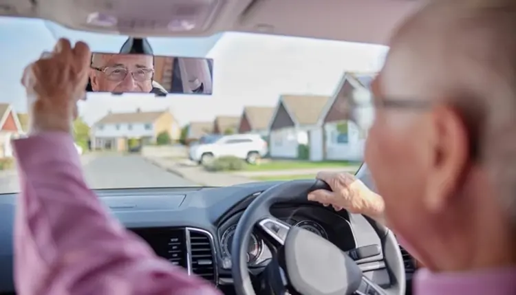 Elderly driver adjusting the rearview mirror while driving through a residential park home estate