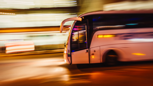 White coach bus speeding through a city at night with motion blur and streaking lights