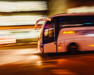 White coach bus speeding through a city at night with motion blur and streaking lights