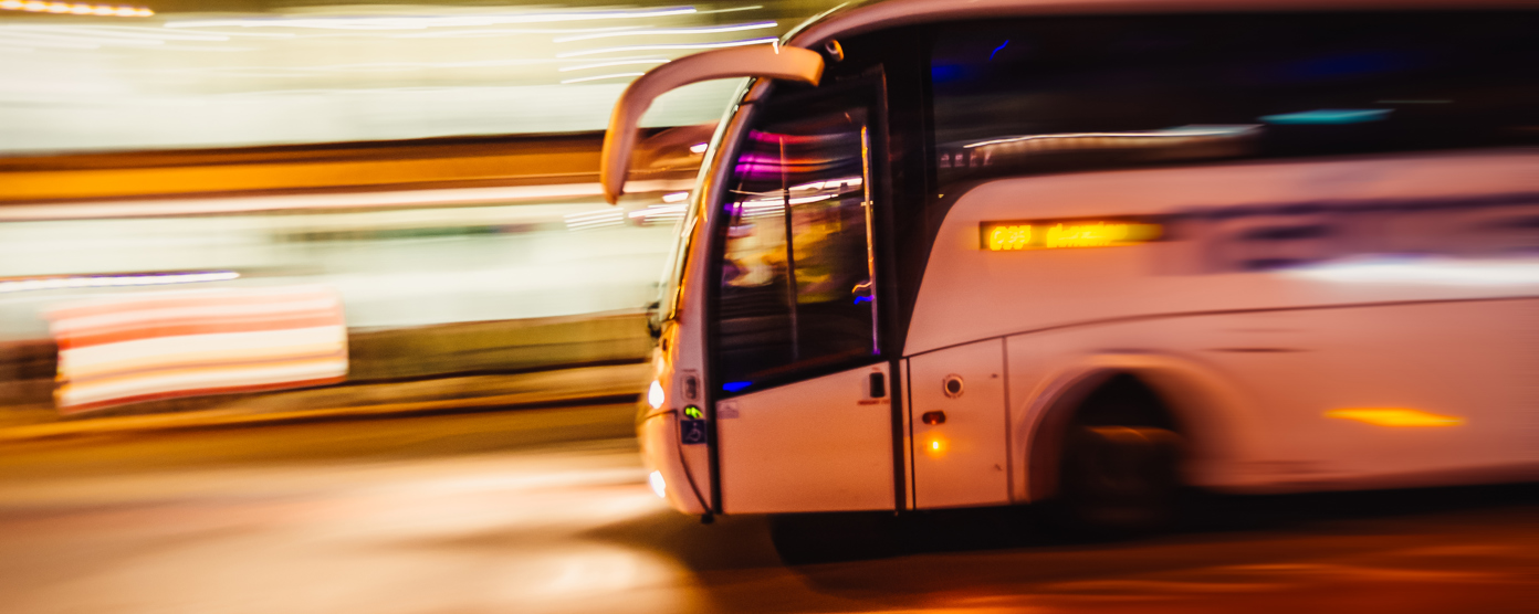 White coach bus speeding through a city at night with motion blur and streaking lights