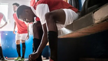 Football player tying shoelace in changing room
