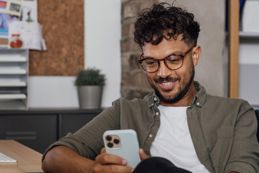 Male with curly hair and glasses smiling at his phone