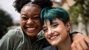 Two females smiling at the camera - one has her arm around the other