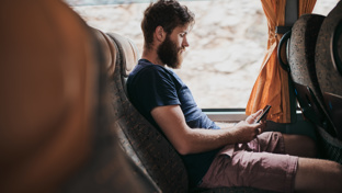 Bearded man sitting on a coach seat, using his smartphone while traveling