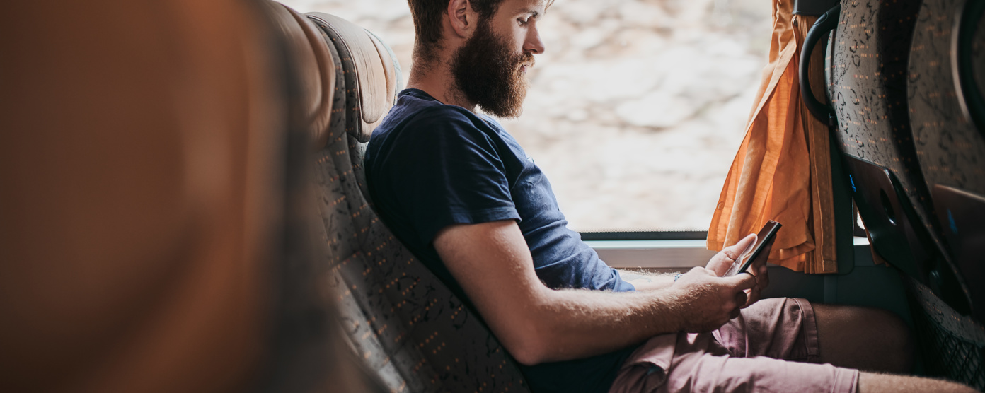 Bearded man sitting on a coach seat, using his smartphone while traveling