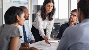Female team leader presenting ideas to a diverse group during an office meeting, pointing at documents on the table
