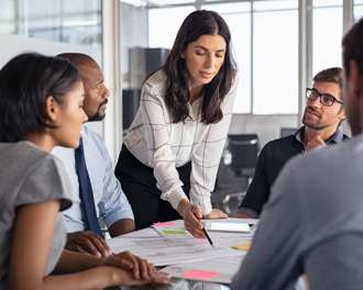 Female team leader presenting ideas to a diverse group during an office meeting, pointing at documents on the table