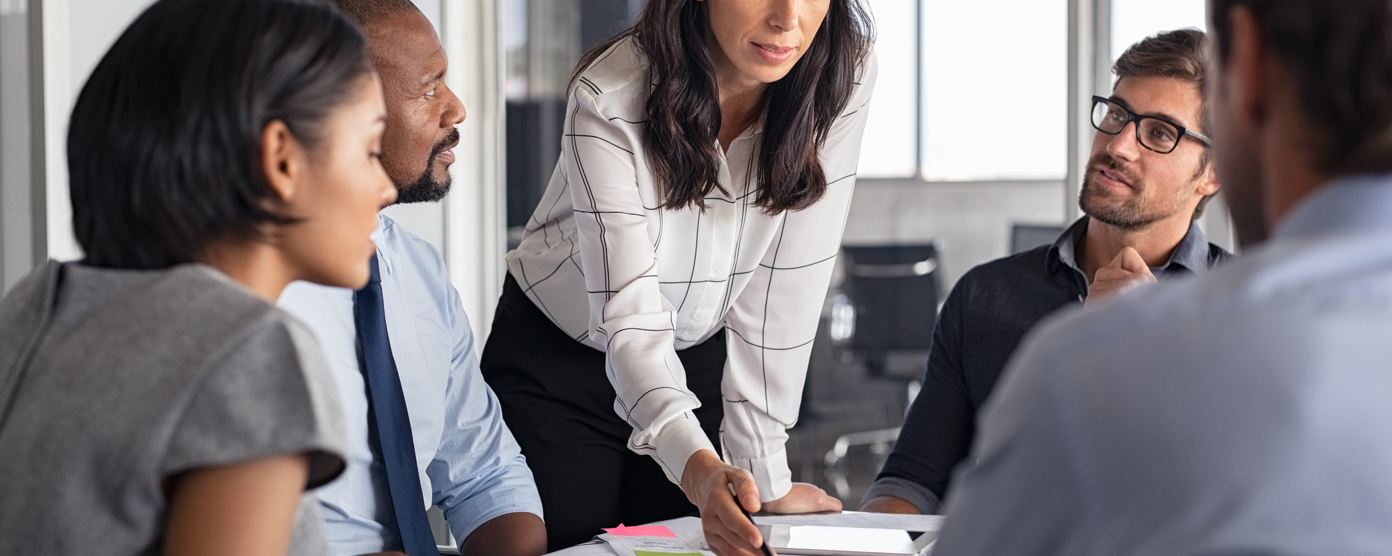 Female team leader presenting ideas to a diverse group during an office meeting, pointing at documents on the table