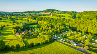 A panoramic aerial view of a vibrant green countryside landscape, featuring gently rolling hills, clusters of trees, and wide open fields.
