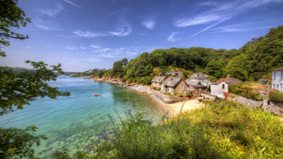 Stone cottages along a small sandy beach, surrounded by lush green hills