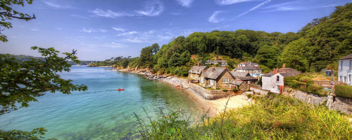 Stone cottages along a small sandy beach, surrounded by lush green hills