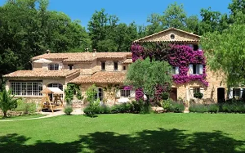 A large rustic-style villa with terracotta roof tiles and stone walls, surrounded by greenery.
