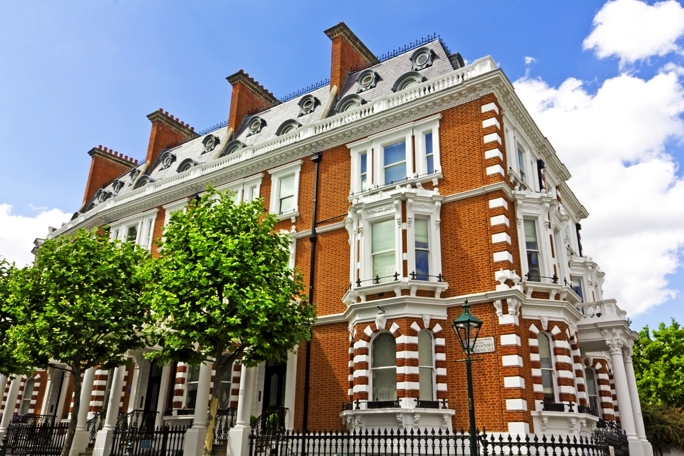 A large Victorian-style redbrick building with ornate white stone trim stands prominently under a bright blue sky with scattered clouds.