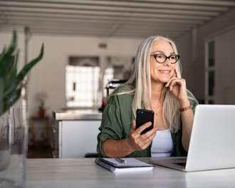 A smiling older woman is sitting at a table in a bright, modern home.