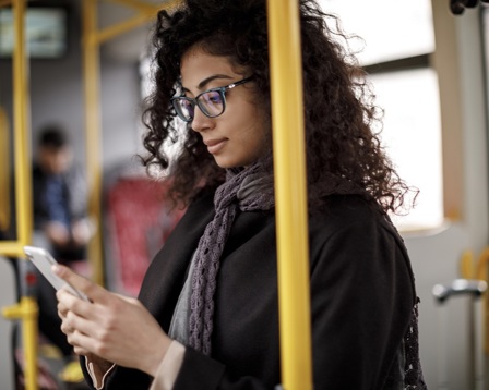 A professional woman in glasses standing on a train looking at her phone
