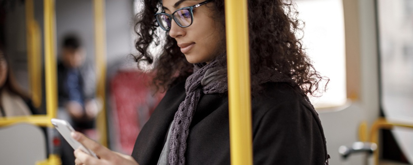 A professional woman in glasses standing on a train looking at her phone