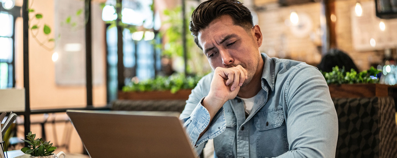 man in light blue jeans problem thinking over a laptop in a cafe