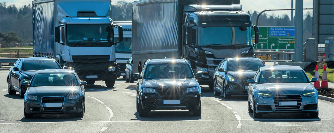 Multiple trucks and cars merging on a motorway in bright daylight with strong sun glare reflecting off windscreens