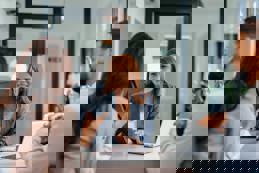 Three business professionals in a modern office meeting discuss a new project, showcasing teamwork and collaboration.