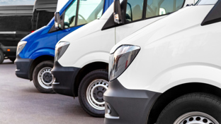 Several white and blue delivery vans lined up closely in an outdoor setting, likely a dealership or fleet parking lot.
