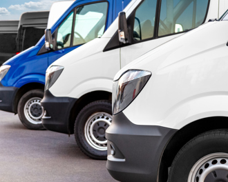 Several white and blue delivery vans lined up closely in an outdoor setting, likely a dealership or fleet parking lot.