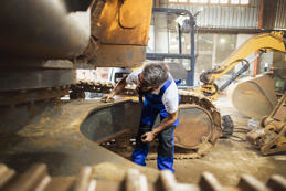 A blue-collar worker uses various tools to tackle a repair on a massive excavator.