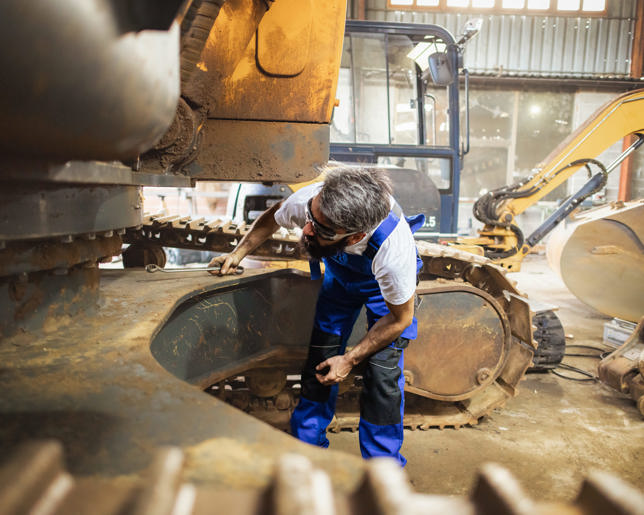 A blue-collar worker uses various tools to tackle a repair on a massive excavator.