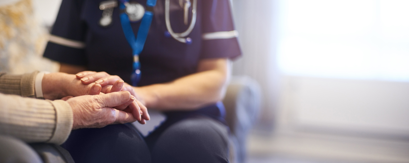  A nurse in uniform compassionately holding the hands of an elderly patient, offering support and comfort in a home or healthcare setting.
