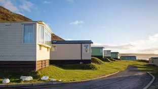 Static caravans lined up on a coastal holiday park at sunset with a winding road and sea views