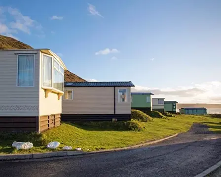 Static caravans lined up on a coastal holiday park at sunset with a winding road and sea views