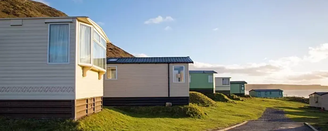 Static caravans lined up on a coastal holiday park at sunset with a winding road and sea views
