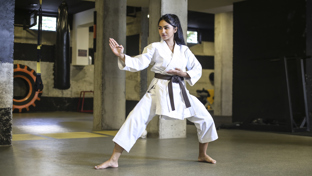 Woman in a white karate gi with a brown belt practicing a defensive stance in a dojo, focused and balanced