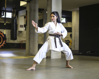 Woman in a white karate gi with a brown belt practicing a defensive stance in a dojo, focused and balanced