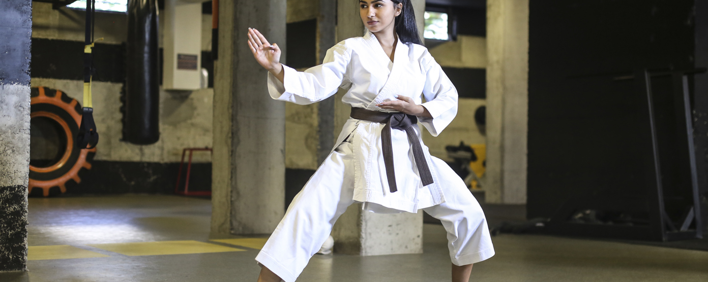 Woman in a white karate gi with a brown belt practicing a defensive stance in a dojo, focused and balanced