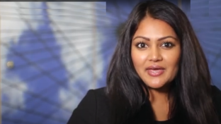 A woman with long, dark hair and medium skin tone is speaking or presenting indoors.