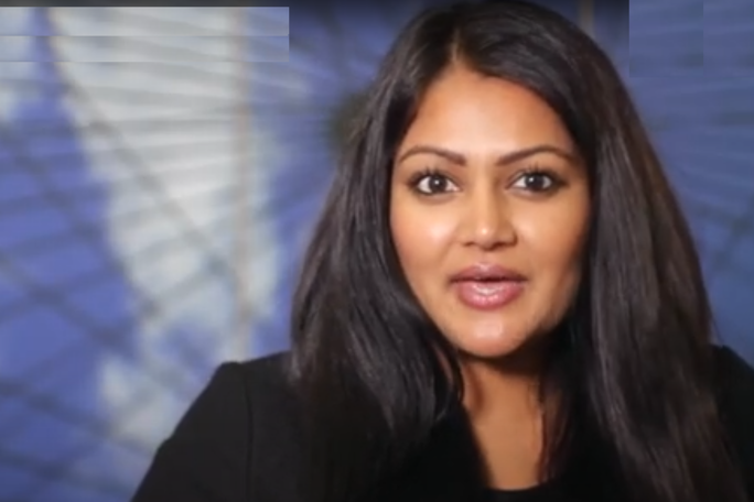 A woman with long, dark hair and medium skin tone is speaking or presenting indoors.