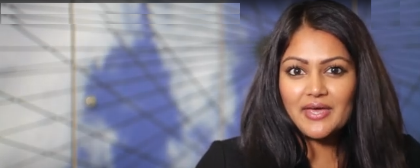 A woman with long, dark hair and medium skin tone is speaking or presenting indoors.