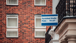 A "Furnished Studio Flats - TO LET" sign mounted on a brick building, indicating available rental.