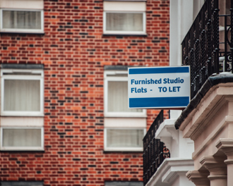 A "Furnished Studio Flats - TO LET" sign mounted on a brick building, indicating available rental.