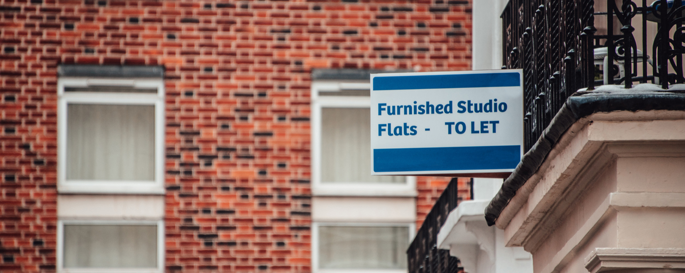 A "Furnished Studio Flats - TO LET" sign mounted on a brick building, indicating available rental.